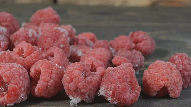 Close-up Of Frozen Raspberries With Dolly Movement. Raspberries Are Sprinkled On A Wooden Table. The Berries Were Taken Out Of The Refrigerator