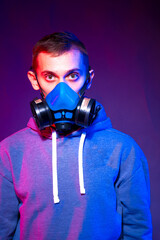 Portrait of an anonymous man, hacker wearing neon mask over dark background. Selective focus of bi-racial cyberpunk player holding guns near neon lighting