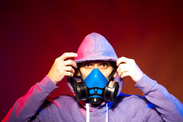 Portrait of an anonymous man, hacker wearing neon mask over dark background. Selective focus of bi-racial cyberpunk player holding guns near neon lighting