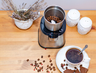Electric coffee grinder grinding coffee beans and standing on the kitchen table, a Cup of black coffee with spices - red pepper and cloves. Morning coffee ritual.