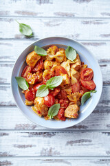 Farfalle pasta with chicken breast, cherry tomatoes and fresh basil. Bright wooden background. Top view. 