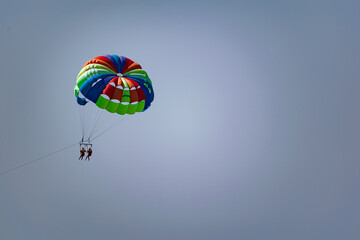 A rainbow-colored striped parachute with two passengers under it. People flying over the blue sea. Entertainment at the resort and active recreation on vacation and on vacation