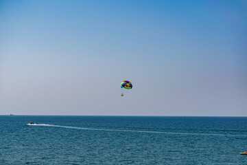 A rainbow-colored striped parachute with two passengers under it. People flying over the blue sea. Entertainment at the resort and active recreation on vacation and on vacation