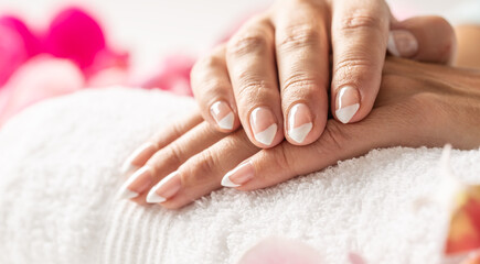 Obraz na płótnie Canvas Nice uncolored nails of crossed hands on a white towel in a nail salon