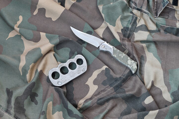 Knife and brass knuckles on a camouflage clothes background. Tools for self-defense or offender...