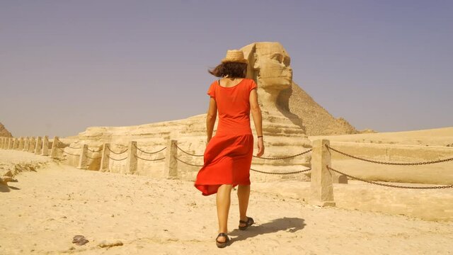 A young Caucasian brunette in a red dress and straw hat enjoying visiting the Great Sphinx of Ginza next to the pyramids of Ginza. Cairo, Egypt