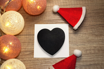 Black heart with space for text among a Christmas garland and two Santa Claus hats. Christmas background