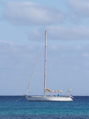Fototapeta premium SANTA MARIA, CAPE VERDE on MARCH 2019: White yacht at Atlantic Ocean landscapes at african Sal island with horizon line and clear blue sky in warm sunny summer day - vertical.