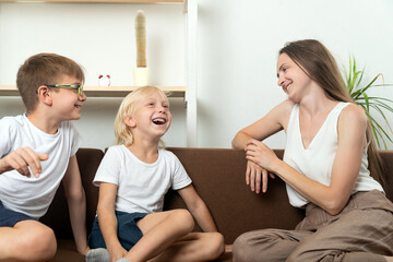 Fototapeta premium Smiling woman and two boys are sitting on couch and have fun talking. Family friendly relations