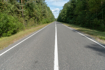 Empty asphalt road through woods and fields. New fresh asphalt pavement away from the city. Development of rural infrastructure. Road marking lines close up.