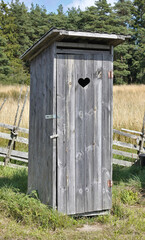 Cute little wooden rustic outhouse with carved heart shape on the door. Typical countryside vacation home toilet. - 397398537