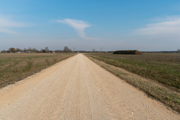 Naklejka premium Empty dirt road through the fields. Fluffy clouds on a warm summer Sunny day over a field of wheat. Pure nature away from the big city. Eco tourism.