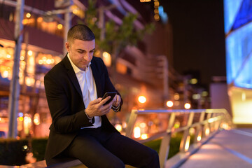 Portrait of businessman using mobile phone at night in the city while sitting