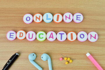 Top view of pen, earphones, pinboards, pink color and alphabet erasers with text ONLINE EDUCATION.