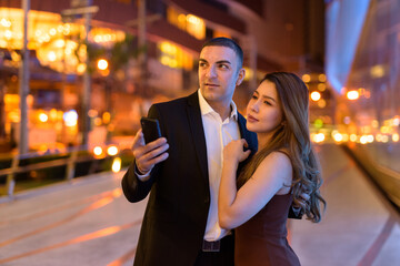 Portrait of couple using phone outdoors at night in the city at Bangkok Thailand