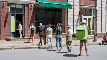 Full length shot of people waiting, standing in line, respecting social distancing to collect their...