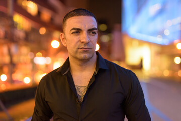 Fototapeta premium Portrait of handsome man with short hair thinking outdoors at night in city