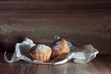 Two cupcakes and a wooden table are illuminated by a beam of light. Image with selective focus.