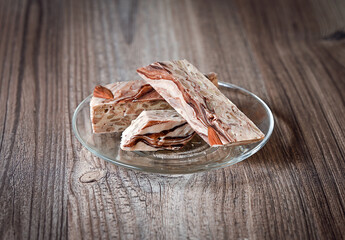 On a wooden table is a transparent saucer with halva. Image with selective focus.