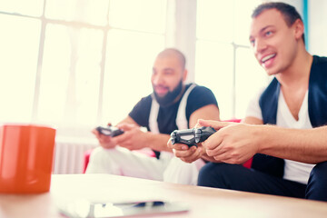 Fototapeta premium Friends and video games. Two handsome young men playing video games while sitting on sofa