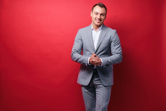 Confident And Charisma. Portrait Of Happy Young Business Man In Suit Looking At Camera While Standing Against Red Wall.