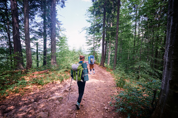 Rear view of two young people walking down the trail path on forest. Young couple hiking with backpacks.