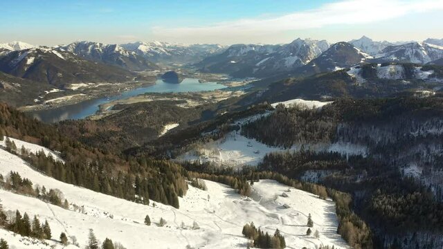 Majestic sunny mountain landscape in winter, aerial footage with gentle forward movement, with evergreen forests, snow covered slopes and a beautiful lake