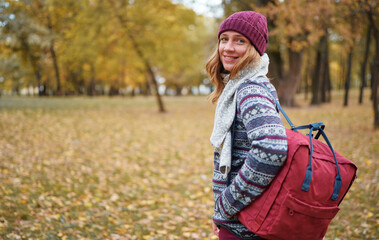 Outdoors portrait of young pretty woman in hat with rucksack in autumn park.