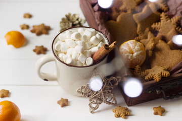Fototapeta na wymiar Christmas coffee cup with marshmallow, christmas cookies, golden star , tangerine in christmas lights.Christmas or new year background on white wooden board