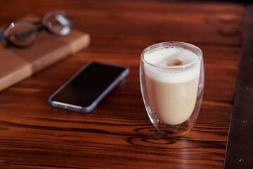 Fototapeta na wymiar Coffee break. Glass of cappuccino, smartphone and book on wooden table.