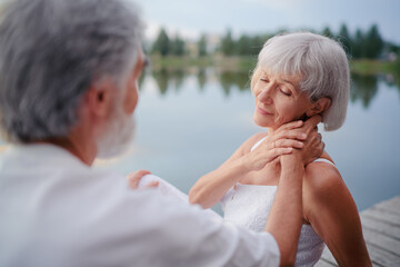 Romantic holiday. Senior loving couple sitting together on lake bank.