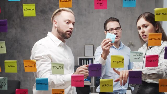 Team of business people is doing brainstorm at a meeting using stickers on the glass. Office workers are discussing strategy, business plan and goals. Startup concept.