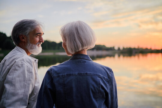 Romantic holiday. Senior loving couple sitting together on lake bank enjoying beautiful sunset.