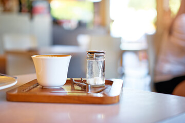 Morning coffee in cozy cafe. White cup of coffee and glass sugar bowl with metal sugar tongs standing on the table.
