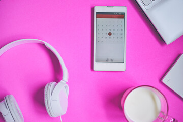 Overhead of modern comfort work place. Different objects on pink background. Items include laptop, earphones, smartphone and cup of milk.