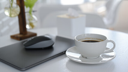 White coffee cup with laptop on white table.
