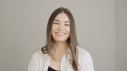 Fototapeta premium Portrait of a laughing young woman. An adult girl in a white medical robe smiling and looking at the camera. Cute brunette with smooth healthy skin and long straight hair.