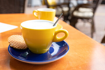 cappuccino in yellow cup. With typical Dutch caramel cookie called Stroopwafel