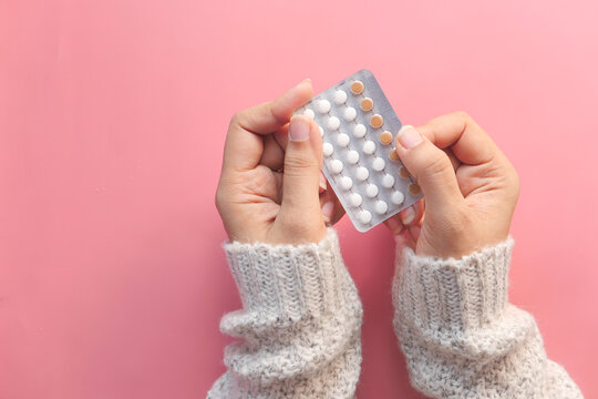 women hand holding birth control pills on pink background 
