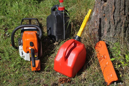 Outdoor chainsaw refueling - motorsaw, special plastic red can with gasoline fiel mix and chain oil canister, lumber sawing equipment near woon trunk at Sunny summer day on green grass background - Powered by Adobe