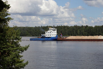 Russian pusher cargo tug ship carries a loaded barge on the Volga river on green forest shore and...
