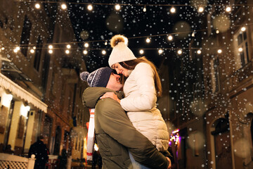 Christmas gifts exchange. Xmas celebration together. Smiling couple celebrating Xmas eve together at bright garland decoration.