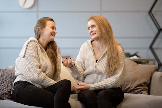 mother and grown-up adult daughter sit on couch in living room have fun talking, happy mature mom and millennial girl child relax on sofa at home together, chat and laughing