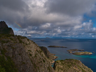 Fototapeta na wymiar Beautiful aerial panoramic view of coast of Norwegian Sea on Austvågøya island near Henningsvær, Lofoten, Norway with rugged mountains and light rainbow on sunny day in late summer with cloudy sky.