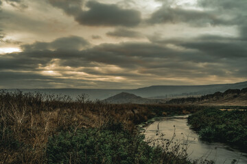 Little river flowing in the countryside. Cloudy sky.