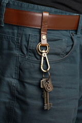 Cropped shot of male body in black shirt and blue jeans with brown belt. Stylish keychain with brown leather belt loop, bronze rings, lobster clasp, charms and keys is fixed on the brown belt. 
