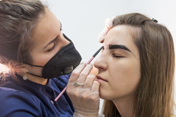 Beautiful young female master makes eyebrow correction procedure.