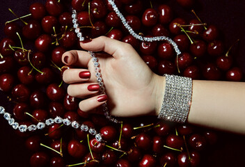 Hand with bright red manicure close-up holds shining necklaces and bracelets with transparent...