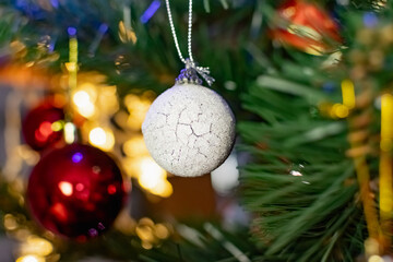 Interesting Christmas toys on the Christmas tree. Christmas accessories in white, among flashing lanterns and lights. Festive and elegant cute things for family holidays.