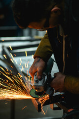 Metal worker in safety googles polishing metallic profile with angle grinder in workshop 